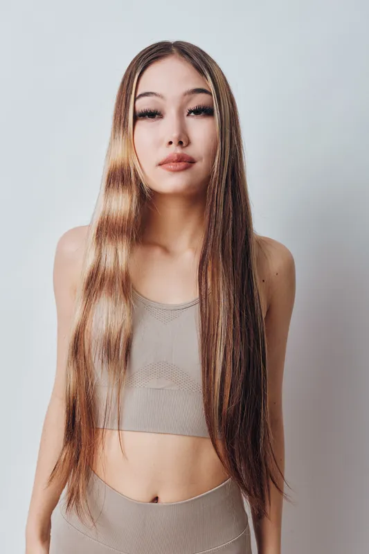 Woman with long straight hair and natural makeup posing in beige crop top and pants against white background in studio. Fashion, beauty and style portrait.
