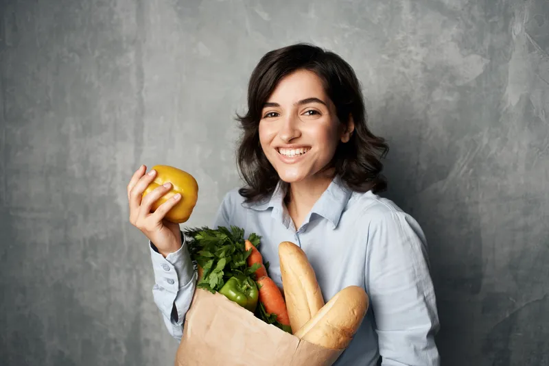 Весёлая брюнетка с сумкой продуктов, овощами и диетическим питанием