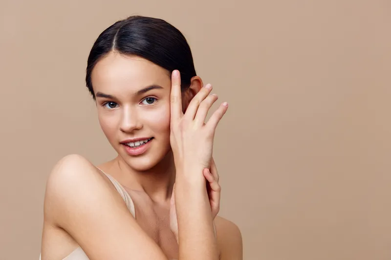 Young woman with a natural smile, showcasing healthy skin against a soft beige background, embodying beauty, freshness, and confidence in a minimalist style