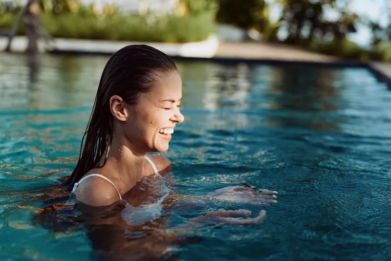 Happy woman enjoys swimming in outdoor pool on sunny day smiling and relaxing with wet hair lifestyle concept leisure and wellness closeup portrait
