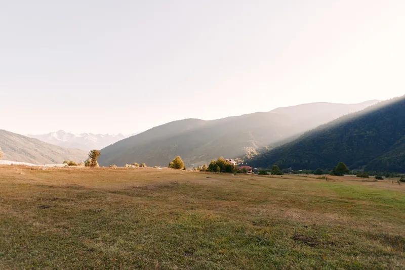 Meadow valley mountains at sunrise over an open field with dry grass and rolling hills, panoramic landscape with soft morning light and distant peaks in peaceful rural scenery.