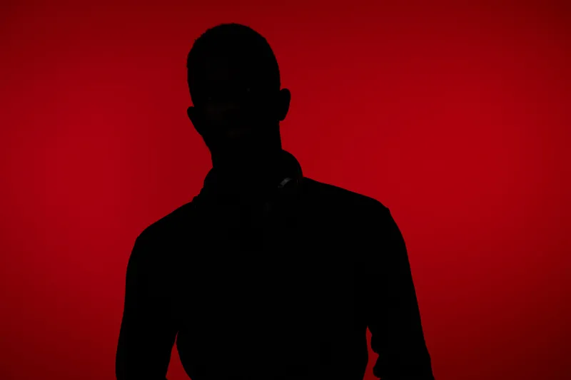 Silhouette of a man with headphones against a striking red background, conveying a mood of mystery and intrigue in a modern aesthetic
