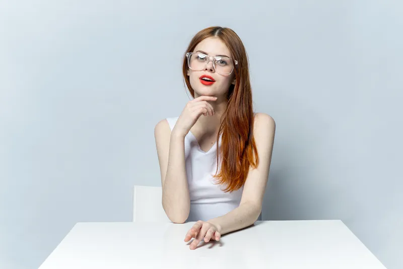 Красивая рыжеволосая женщина в очках сидит за столом