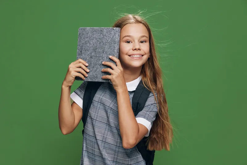 Girl, child, and teenager smiling with book on green background for education, knowledge, and school. Happy kid, learning, reading with backpack for study and student development.