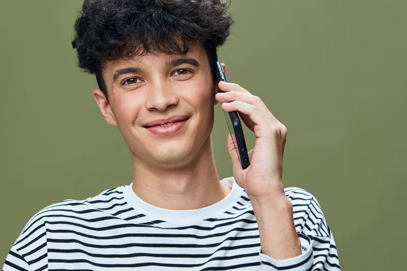 smiling man wearing striped shirt talking on smartphone with green background, casual style, youthful expression, communication concept