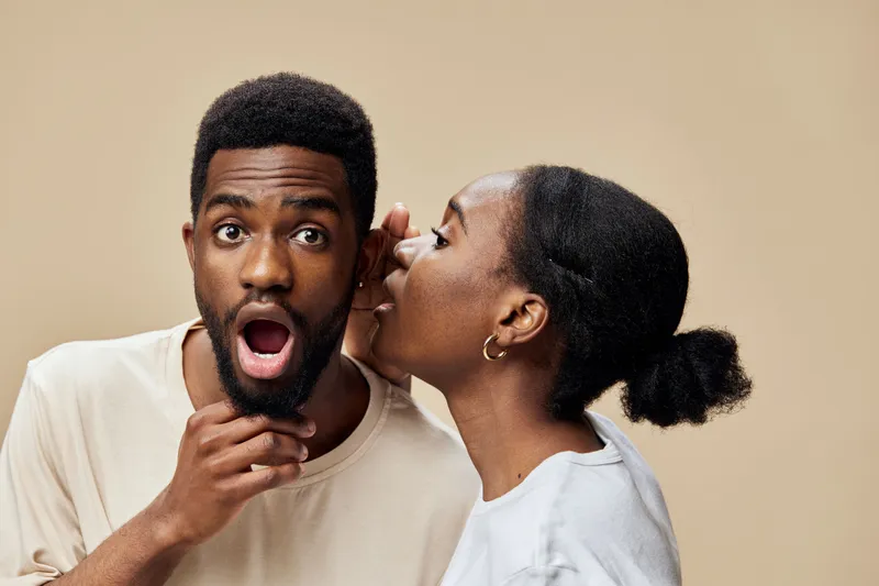 Surprised man and woman having a secret conversation in a neutral toned setting, showcasing emotions of surprise and intrigue