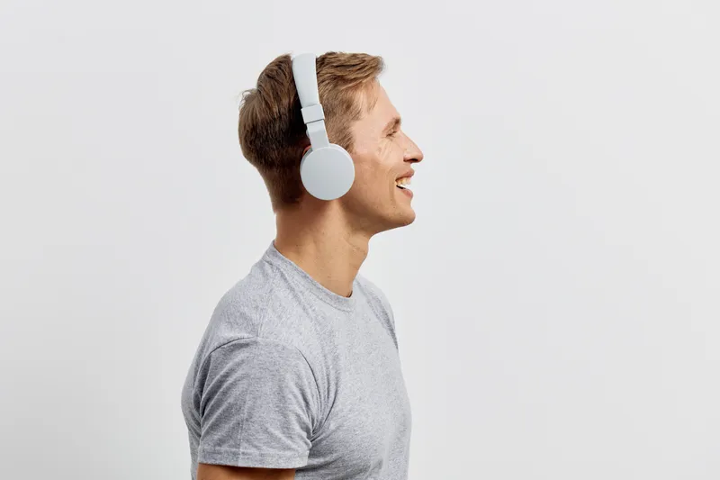 Friendly young Caucasian man wearing large white headphones, smiling and enjoying music, standing sideways in front of a plain white background. Casual lifestyle portrait, positive emotions, leisure c
