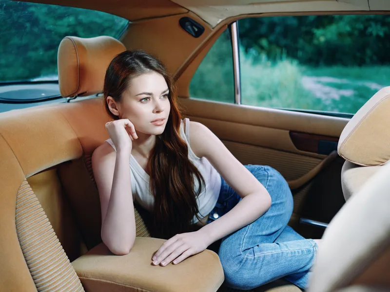 Relaxed young woman in denim jeans, lounging in a vintage car, exuding tranquility and contemplation in a nature setting with soft natural light.