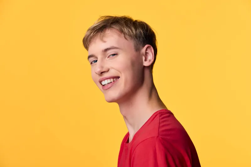 Smiling young male in a red shirt against a vibrant yellow backdrop, casual style and bright mood for lifestyle, fashion and positive energy stock imagery, high key lighting, approachable vibe
