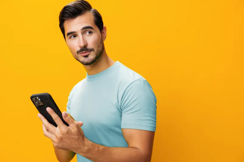 Мужчина в очках держит желтый смартфон, стоя в студии
