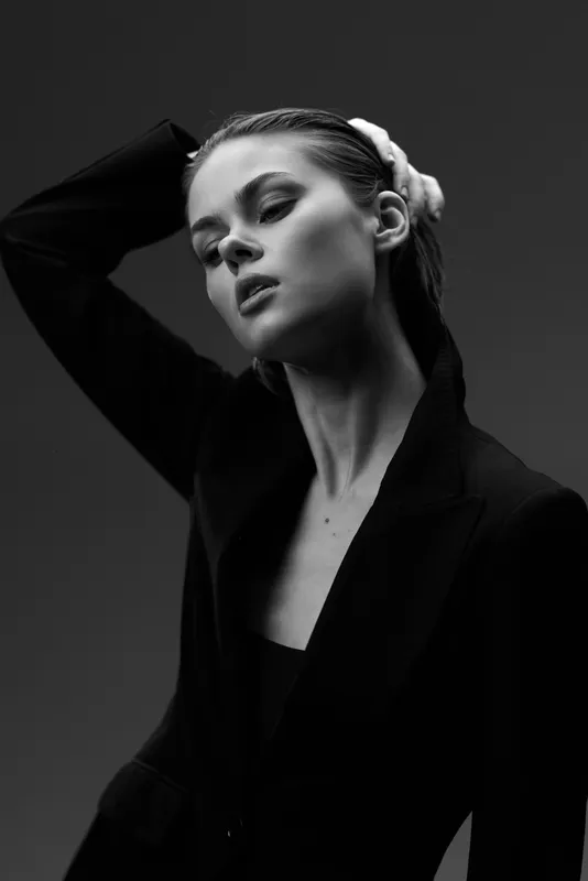 Black and white portrait of a young woman in a dark jacket with a thoughtful expression and elegant pose.