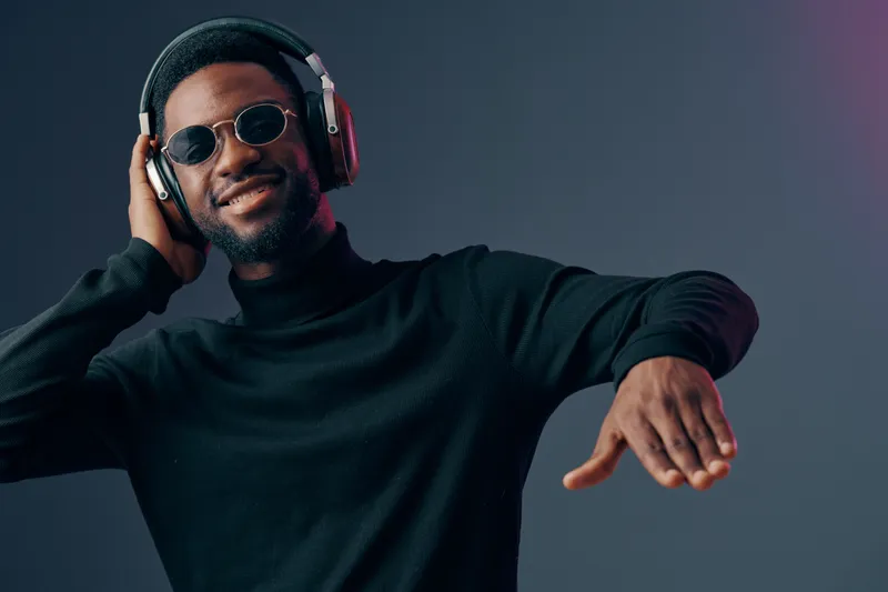 Young Black man enjoying music with headphones on a gradient background, showcasing vibrant emotions and stylish attire, perfect for music related themes