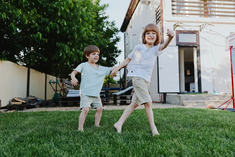 Happy children playing together in a sunny backyard, enjoying their carefree time outdoors in a vibrant green garden. Perfect for family-themed visuals.