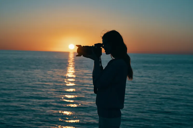 Женщина-фотограф с камерой на закате у моря, на пляже