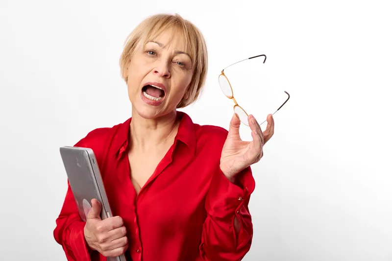 Surprised woman in red shirt holding smartphone and glasses on white background, shocked emotion in studio, copy space, indoor lifestyle, closeup portrait