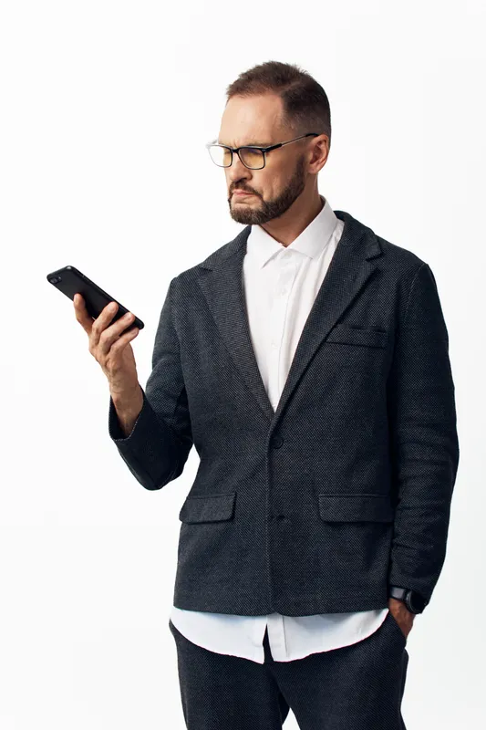 A professional business man in a sharp suit stands, calm yet focused, viewing a smartphone with confident expression against an isolated colored background.