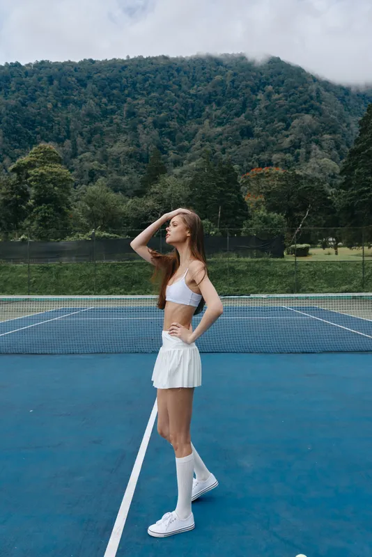 Young female tennis player in sporty attire enjoying a moment on the court, showcasing athleticism and confidence against a natural background, perfect for sports related themes