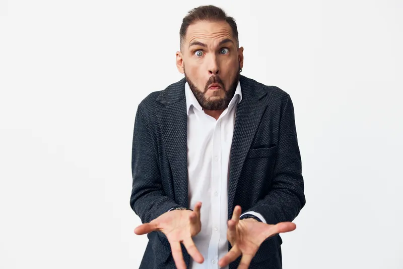 A professional businessman stands against an isolated colored background, conveying emotion and confidence. The image captures a surprised moment and ready posture, highlighting leadership for