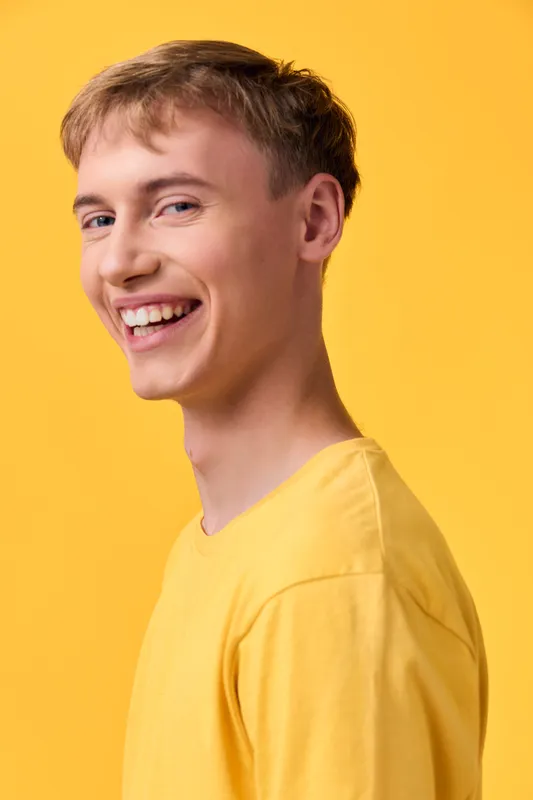 Smiling young man in a yellow shirt stands in a bright studio, cheerful expression and casual fashion captured for lifestyle photography, creating a positive vibe for branding and advertising