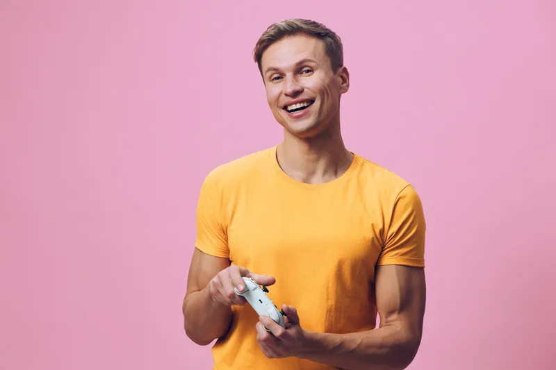 Smiling woman holding game controller, enjoying gaming session, bright yellow t-shirt, pink background, people, hobbies, entertainment, lifestyle, fun, modern society, leisure activity, casual, joyful