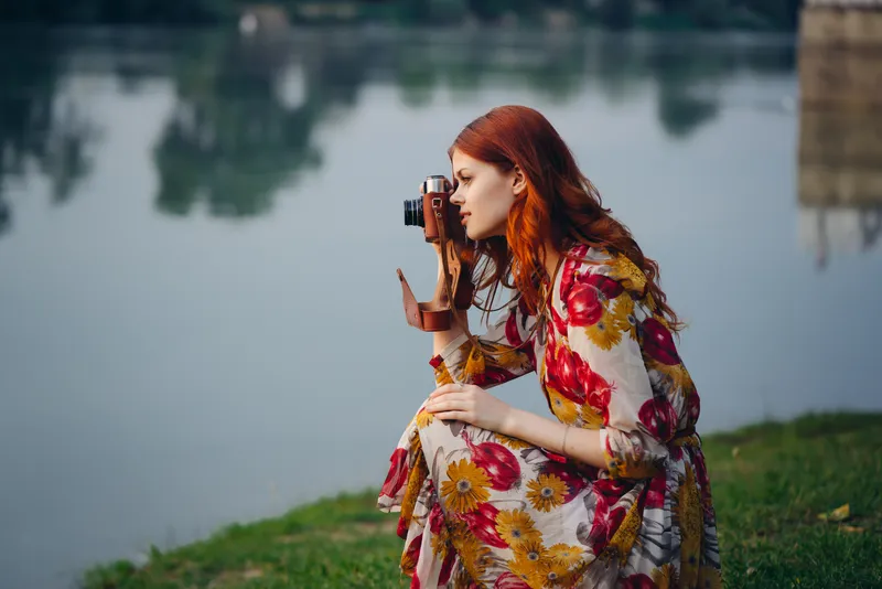 Женщина в платье с фотоаппаратом на природе, снимающая реку как хобби