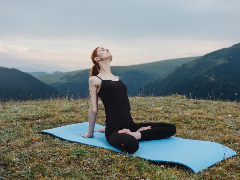 Спортивная женщина в горах занимается йогой и фитнесом на открытом воздухе, выполняя упражнения