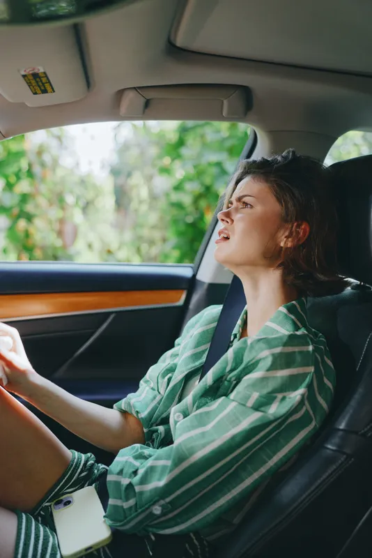 A woman driver sits in the car seat with focus and ease, hands on the steering wheel as sunlight highlights her face.