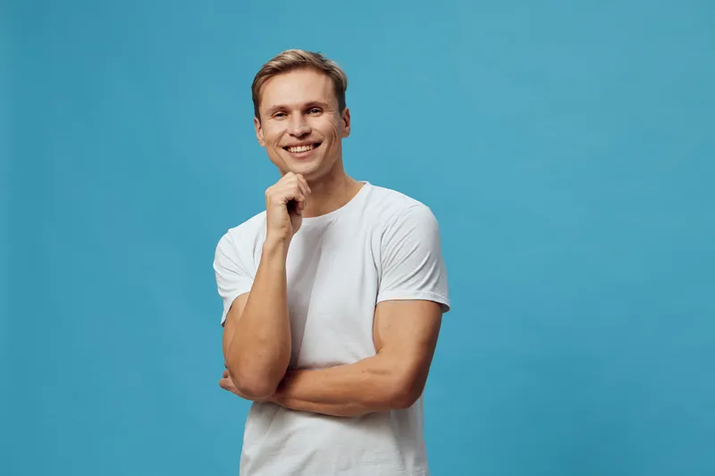 Confident young Caucasian man smiling with funny pose, wearing casual white t-shirt, standing against vibrant blue background, studio portrait, cheerful expression, lifestyle concept, male, happiness,