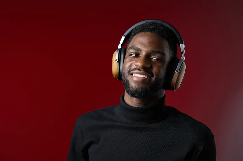 Young Black man smiling while wearing headphones against a red background, exuding joy and style, ideal for music and lifestyle themes