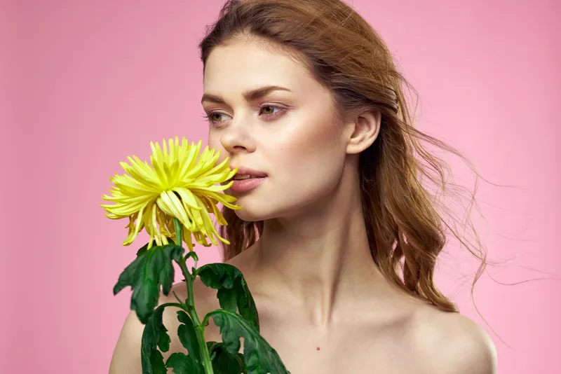 Красивая девушка с жёлтым цветком на розовом фоне, обнажённые плечи, макияж