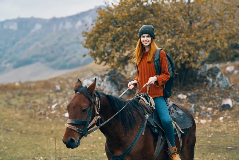 Женщина-туристка с рюкзаком едет верхом на лошади в горах, путешествуя на природе