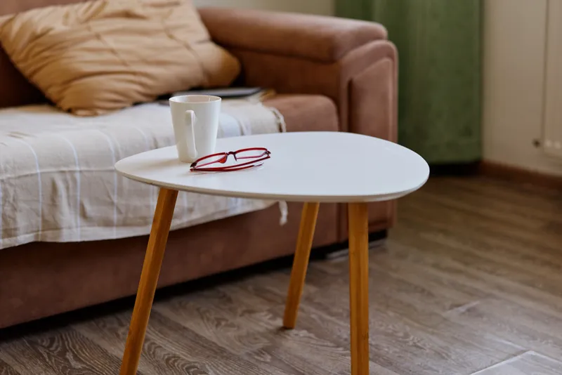Calm living room scene with a round white coffee table, a mug and red glasses resting on its surface, and a sofa in the background, creating a cozy home mood and simple interior detail.