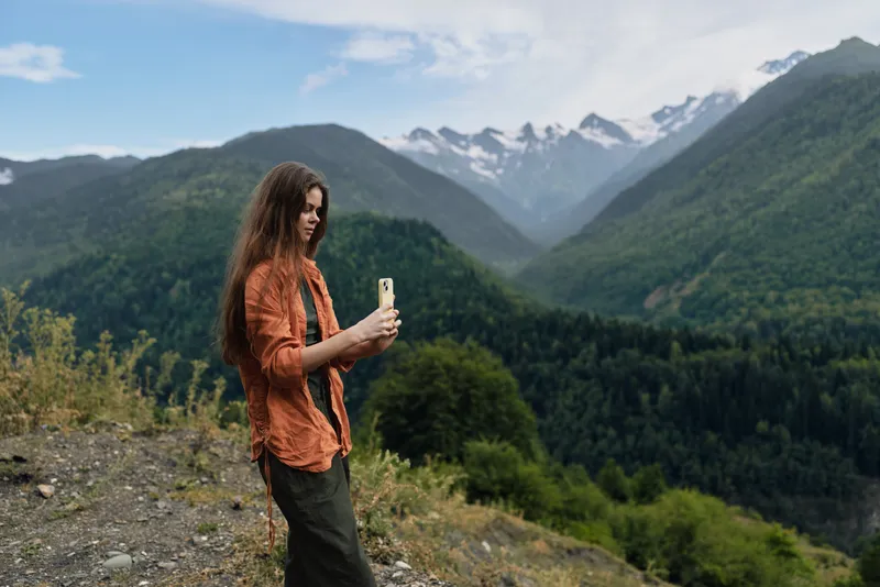 Woman hiking in mountains with phone taking photo of nature landscape outdoors travel scene authentic inclusivity and calm