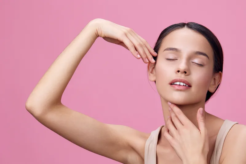 A young woman of Latin descent poses gracefully against a pink background, showcasing natural beauty and serenity, emphasizing self care and skin health