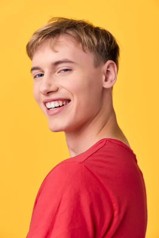Smiling man in a red shirt stands against a bright yellow backdrop, radiating carefree energy and friendliness, ideal for lifestyle, fashion, or advertising campaigns