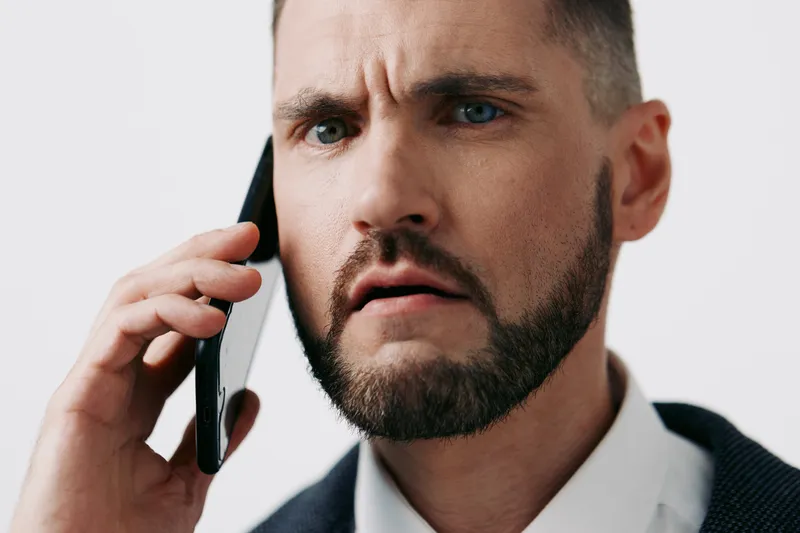 A focused business professional on a mobile call, portrait against a solid colored backdrop, conveying urgency and concern during a critical conversation.