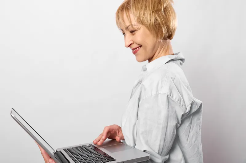 Woman on laptop, technology for remote work, typing and communication, smile in side profile on plain white background. Home office productivity concept.