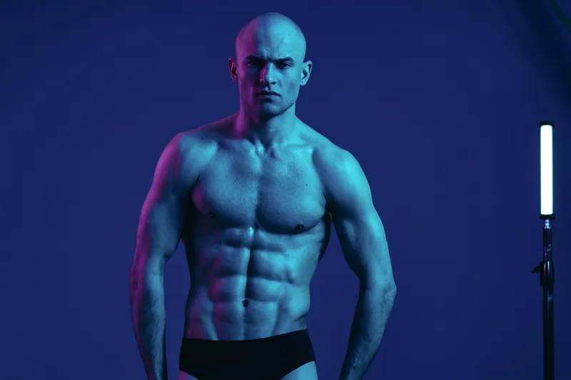 Athletic man posing confidently in a cool-toned, colorful light. The strong silhouette and striking colors create a dynamic atmosphere in the scene.