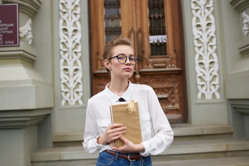 Коротко стриженная женщина в очках прогуливается по городу с книгой в руках