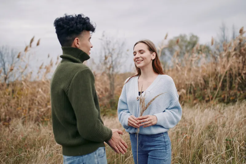 Two individuals share a candid conversation in a natural field, presenting authentic connection and credibility through relaxed stance, sincere smiles, and everyday interaction.