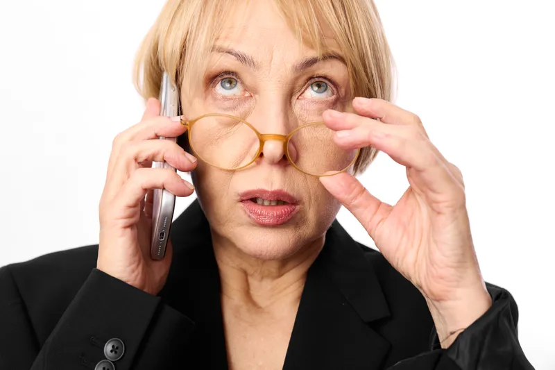 Senior woman business glasses phone smartphone surprise stress on her face, she holds smartphone for a phone call, communication concern, isolated portrait on white background