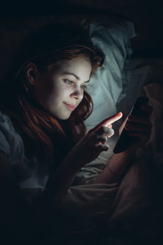 Улыбающаяся женщина с телефоном в руках ночью лежит в постели, образ жизни, общение