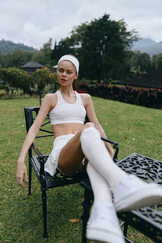Outdoor portrait of a young model in sporty white outfit, showcasing athleticism and confidence in a green park setting with soft daylight