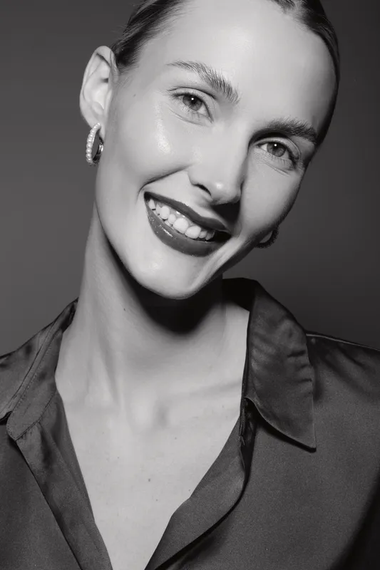 Smiling Caucasian woman with light skin and earrings in satin blouse poses in black and white studio portrait. Concept of beauty, happiness, and elegant fashion.