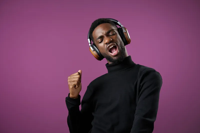 Young Black man enjoying music while dancing against a purple background, expressing joy and energy with stylish headphones