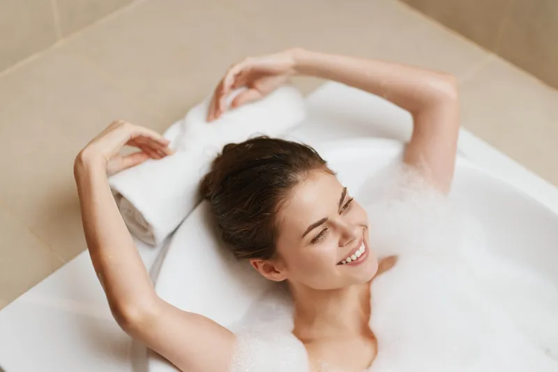 Веселая женщина нежится в роскошной пенной ванне, излучая счастье, с полотенцем, свернутым под головой, создавая спокойную и восстанавливающую атмосферу