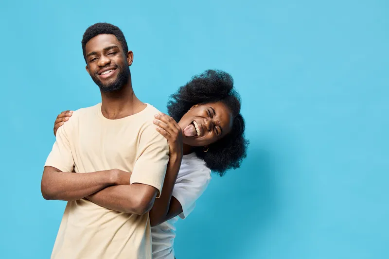Happy young African American couple posing together against a blue background, showcasing joy and playfulness in a casual style