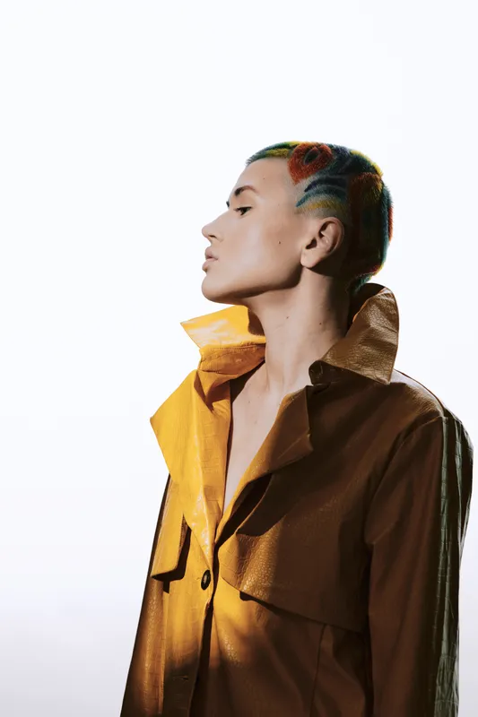 woman with colorful short hair wearing a stylish brown coat, profile view, minimalistic white background, modern fashion, artistic lighting