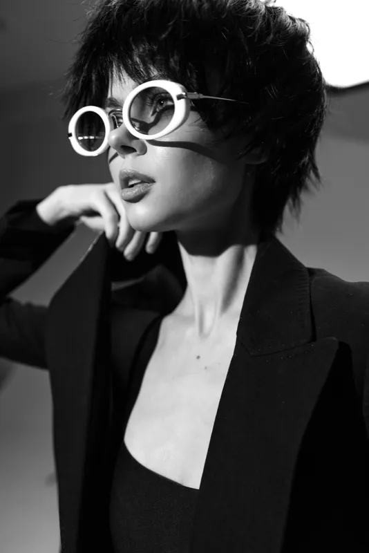 Stylish woman with short hair wearing round sunglasses in black and white portrait, emphasizing fashion and modern elegance.