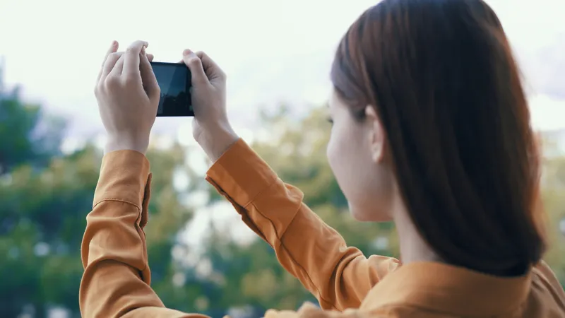 Женщина на улице с телефоном в руках фотографирует на камеру